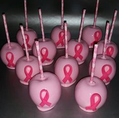 pink apples with pink ribbon on them are lined up in rows and have candy sticks sticking out of them