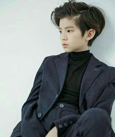 a young man sitting on the ground wearing a suit and turtle neck sweater with his hands in his pockets