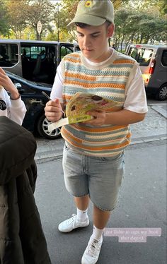 a young boy is holding a sandwich and looking at his cell phone while walking down the street