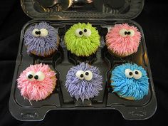 cupcakes with googly eyes are in a plastic container on a black background