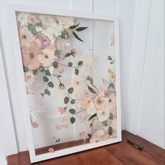 a white frame with flowers on it sitting on a wooden floor next to a wall