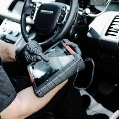 a man in black gloves is holding a tablet and sitting in the driver's seat of a car