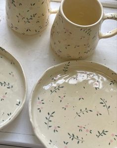 two white plates with flowers on them next to a coffee cup and saucer sitting on a window sill