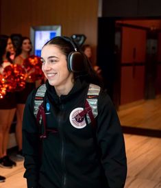 a woman wearing headphones standing in front of cheerleaders at a dance event