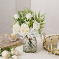 a vase filled with white flowers sitting on top of a table next to two candles