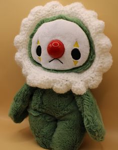 a green stuffed animal with a red nose and big eyes sitting on a brown surface