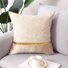 a coffee cup and saucer on a gray couch next to a potted plant