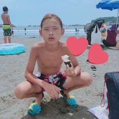 a young boy sitting on top of a sandy beach next to the ocean holding a piece of cake