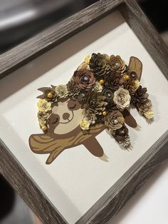 a wooden frame with paper flowers in the shape of a teddy bear and pine cones