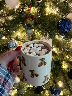 someone holding a cup of hot chocolate in front of a christmas tree