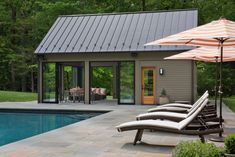 two lounge chairs and an umbrella are by the swimming pool in front of a house