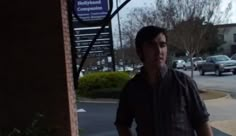 a man standing on the sidewalk in front of a building with cars parked behind him