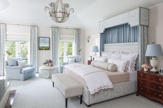 a bedroom with a bed, chair and chandelier hanging from the ceiling in front of two windows