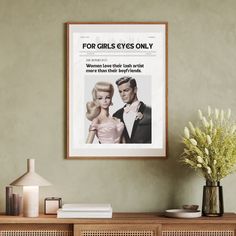 a framed poster hangs on the wall next to a vase with flowers