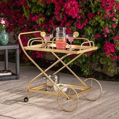 a gold serving cart with drinks on it sitting in front of some pink and purple flowers