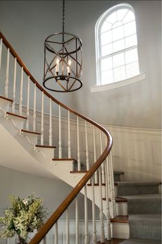 a spiral staircase with two lights hanging from the ceiling and flowers in vases on either side