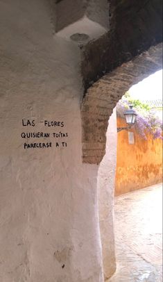 a white wall with writing on it in an alley way next to a lamp post