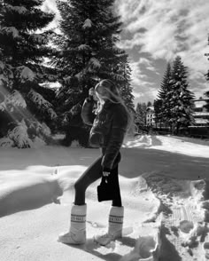 a woman standing in the snow with her legs crossed and boots on, drinking from a cup