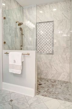 a bathroom with marble walls and flooring, white towels hanging on the shower door