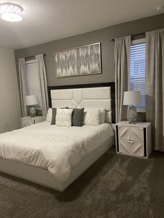 a large white bed sitting in a bedroom next to two windows