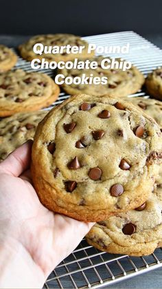 a hand holding a chocolate chip cookie on a cooling rack