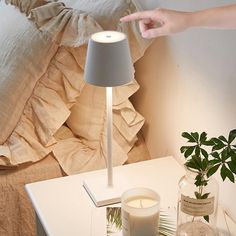 a white table with a lamp, candle and pictures on it next to a bed