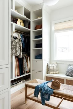 an open closet with clothes and shoes on the floor, next to a bench in front of a window