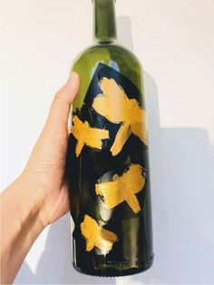 a hand holding a wine bottle with gold paint on it