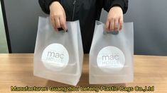 a person holding two plastic bags with the logo mac house on one side and another bag in the other