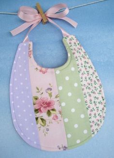 a bib hanging on a clothes line with a pink bow around the neck and two different colors of bibs