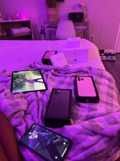 several cell phones are laying on a bed with purple lights in the room behind them