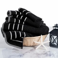 black towels in a basket next to a lantern and starfish on a white background