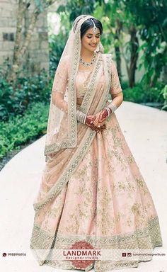 a woman in a pink and gold bridal gown standing on a path with greenery behind her