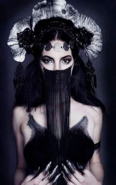 a woman with long black hair and makeup holding a fan in her hands, wearing an elaborate headdress