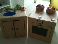 two cardboard play kitchen sets sitting on the floor