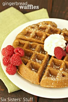 a white plate topped with waffles covered in powdered sugar and raspberries