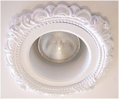 a white ceiling light with an ornate design on the top and bottom, mounted in a wall