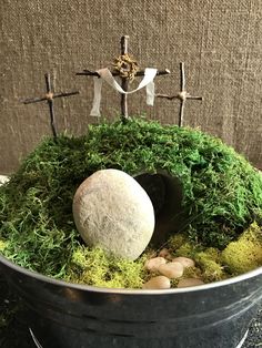 a bucket filled with moss and rocks on top of a table next to a cross