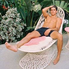 a man sitting in a wicker chair with his feet up on a pink table