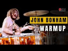 a man with long hair playing drums in front of a yellow sign that says john bonhan warm warm up