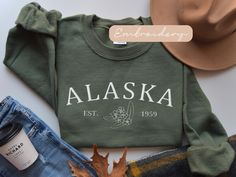 Embrace the spirit of the Last Frontier with our meticulously embroidered Alaska sweatshirt, a cozy tribute to the wild and beautiful North. Stay warm and show your love for Alaska in style with this must-have addition to your wardrobe. ✨DESCRIPTION✨  🌟GILDAN 18000 Unisex Sweatshirt - Embroidered design *100% cotton (Sport Grey is 90% cotton, 10% polyester; Ash Grey is 99% cotton, 1% polyester, heather colors are 50% cotton, 50% polyester. *Sweatshirts are in UNISEX sizing. Select your usual size for a more fitted look, or size up for a more relaxed fit. *Please note that the embroidery design has a backing on the inside of the sweatshirt to support the fabric and stitches. *Fabric Weight 5.0-5.3 oz/yd² (170-180 g/m²) *pre-shrunk jersey knit, air jet spun yarn for a soft feel & reduced pi Alaska Sweatshirt, Alaskan Vacation, Alaska Moose, Elizabeth Bennet, Family Cruise, Alaska Cruise, Womens Sweater, Sweater Gift, Family Trip