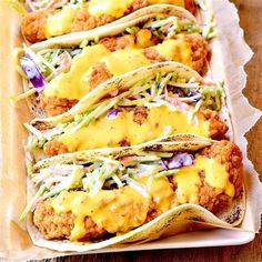 three tacos with chicken and coleslaw are lined up on a paper tray