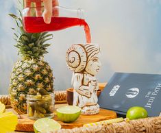 a pineapple is being poured into a glass in front of a wooden carving of a woman