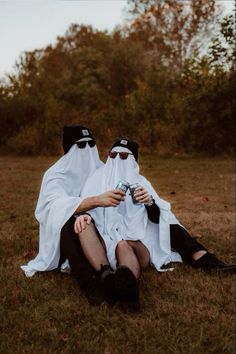 two people dressed in black and white sitting on the ground with their heads covering each other