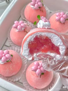 pink desserts with white frosting and flowers on them are in a tray, ready to be eaten