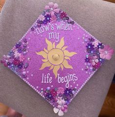 a purple and yellow graduation cap with flowers on the front that says, flows when my life begins