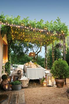 an outdoor dining area with potted plants and lights strung from the roof over it