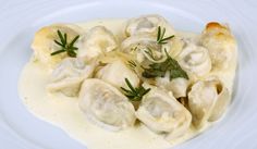 a white plate topped with dumplings covered in sauce and garnished with herbs