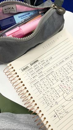 an open notebook sitting on top of a table next to a pencil bag and pen