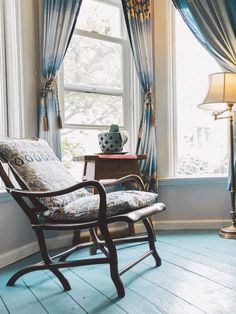 a rocking chair sitting in front of a window next to a table with a lamp on it